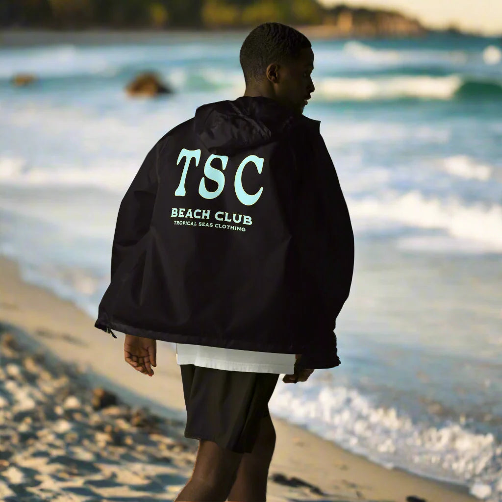 Sustainable Fall Favorites collection at Tropical Seas Clothing, featuring beach-ready, eco-conscious styles for ocean lovers. Person wearing fall-inspired tropical apparel overlooking a scenic coastline at sunset.