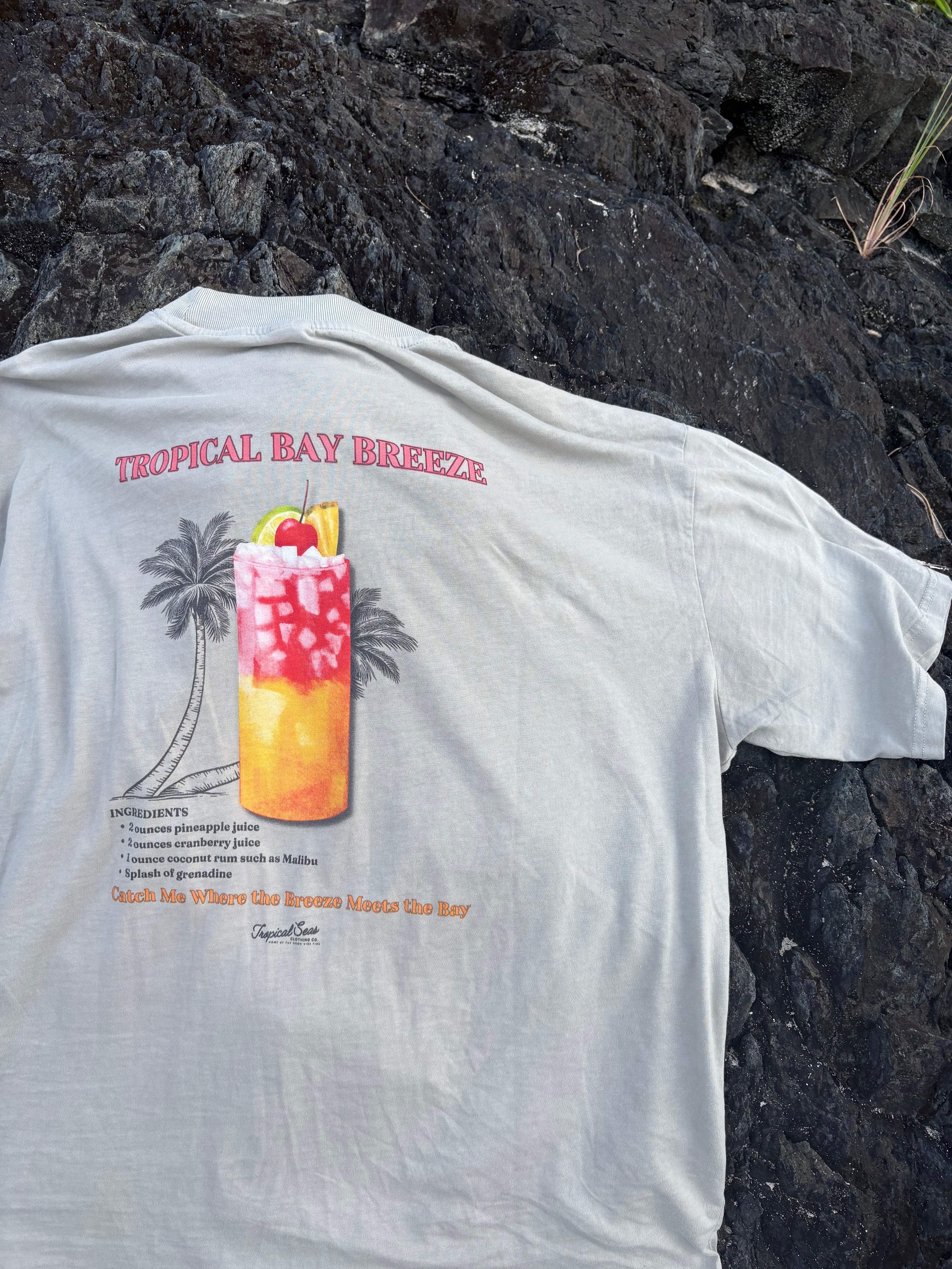 Grey Tropical Bay Breeze t-shirt featuring tropical drink cocktail graphic with palm trees photographed on volcanic rock